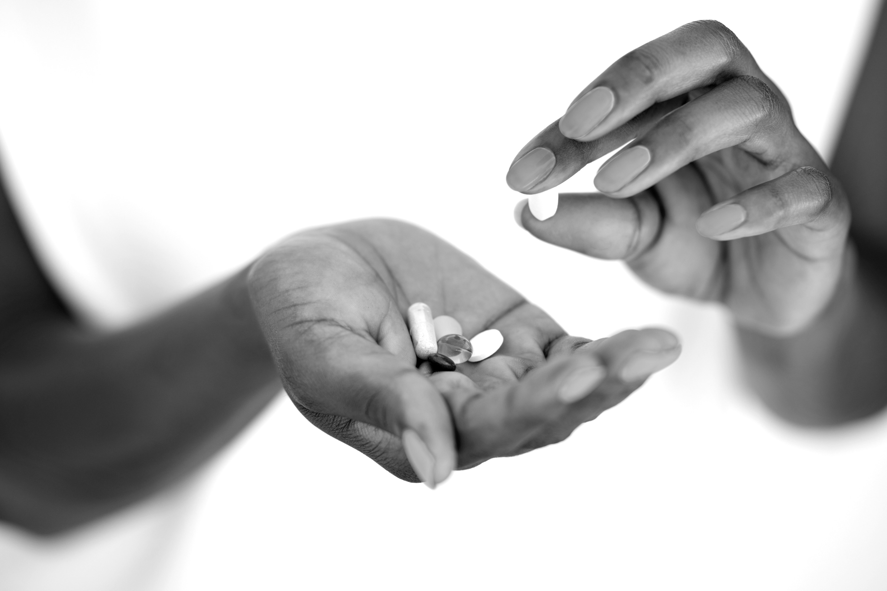 Black-and-white photograph of one hand holding several loose pills while a second hand places another pill into it